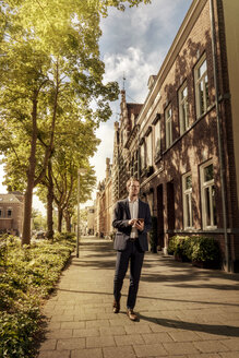 Niederlande, Venlo, Geschäftsmann mit Mobiltelefon auf dem Bürgersteig - KNSF02413