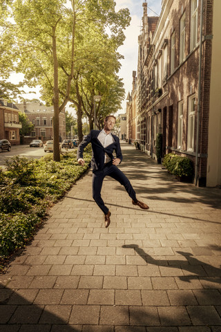 Niederlande, Venlo, glücklicher Geschäftsmann, der auf den Bürgersteig springt, lizenzfreies Stockfoto