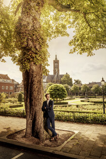 Niederlande, Venlo, Geschäftsmann lehnt an einem Baum - KNSF02415