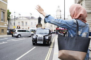 UK, England, London, junge Frau mit Hidschab, die ein Taxi ruft - IGGF00128