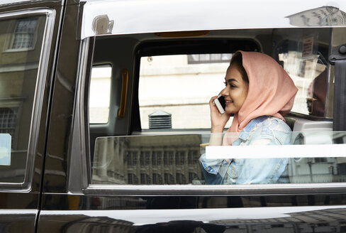 UK, England, London, junge Frau mit Hidschab am Telefon in einem Taxi - IGGF00129