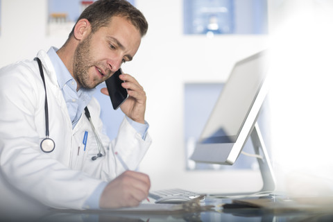 Arzt am Schreibtisch, der mit seinem Handy telefoniert, lizenzfreies Stockfoto