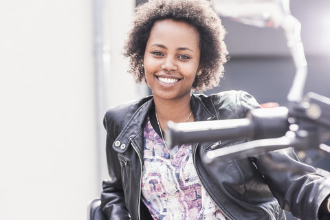 Porträt einer lächelnden jungen Frau mit ihrem Motorrad, lizenzfreies Stockfoto