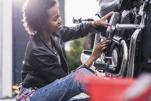 Junge Frau, die ihr Motorrad wartet - UUF11576