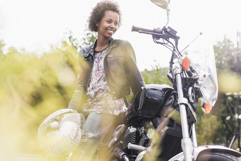 Lächelnde junge Frau mit ihrem Motorrad - UUF11580