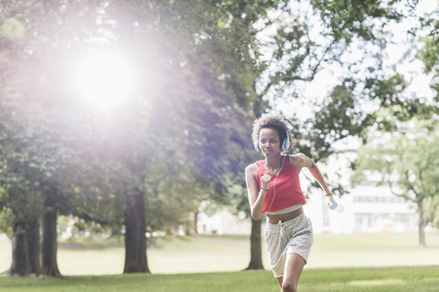 Junge Frau mit Kopfhörern läuft im Park, lizenzfreies Stockfoto