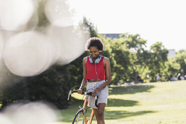 Smiling sporty young woman pushing bicycle in park - UUF11591