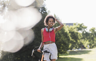 Smiling sporty young woman with bicycle in park - UUF11592