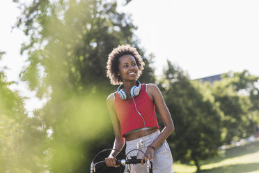 Smiling sporty young woman with bicycle in park - UUF11593