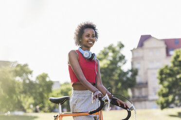 Smiling sporty young woman with bicycle in park - UUF11594