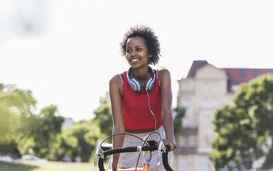 Smiling sporty young woman on bicycle in park - UUF11595