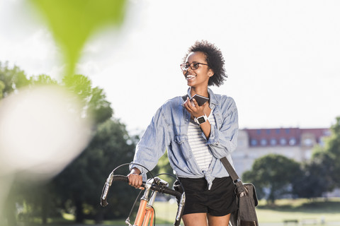 Lächelnde junge Frau mit Handy und Fahrrad im Park, lizenzfreies Stockfoto