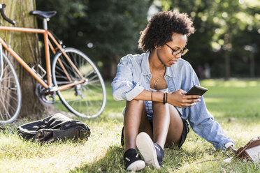 Junge Frau ruht sich im Park mit Handy und Tablet aus - UUF11614