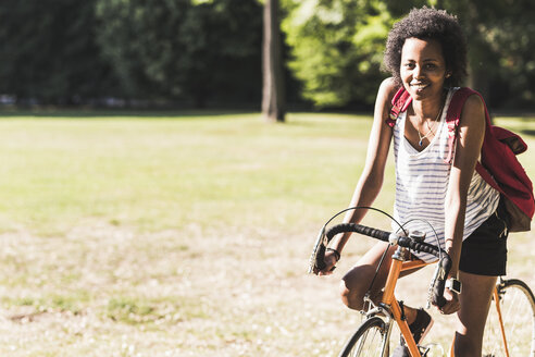 Porträt einer lächelnden jungen Frau auf einem Fahrrad im Park - UUF11616
