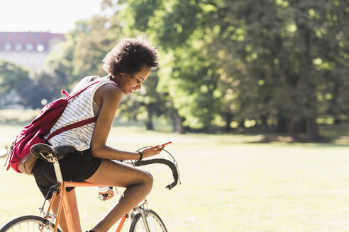 Junge Frau auf dem Fahrrad im Park, die ihr Handy überprüft - UUF11621