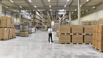 Businessman with laptop standing in warehouse - LYF00760