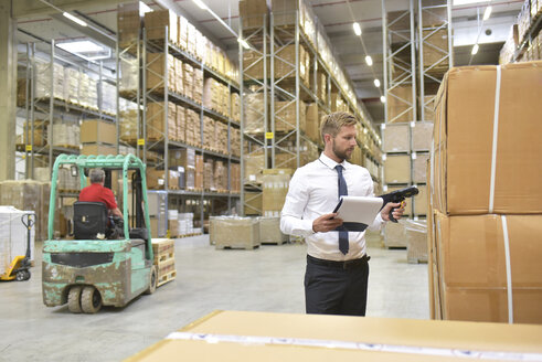 Businessman with clipboard in warehouse scanning goods - LYF00766