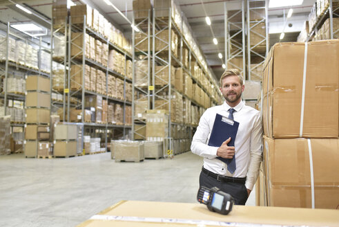 Confident businessman with clipboard and barcode scanner in warehouse - LYF00767