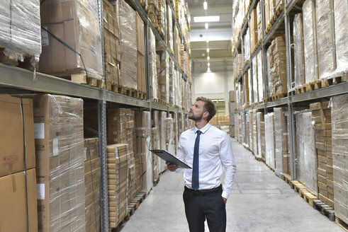 Businessman with clipboard in warehouse looking at shelves - LYF00770