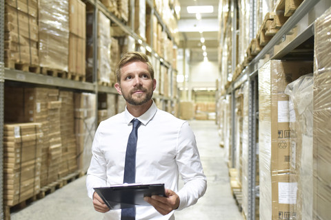 Businessman with clipboard in warehouse looking at shelves stock photo