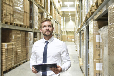 Businessman with clipboard in warehouse looking at shelves - LYF00773