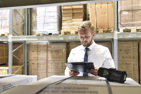 Geschäftsmann mit Klemmbrett und Barcode-Scanner im Lager, lizenzfreies Stockfoto