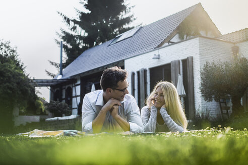 Glückliches reifes Paar auf der Wiese vor ihrem Haus liegend - RIBF00670