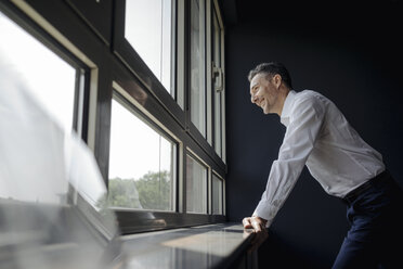 Lächelnder Geschäftsmann im Büro und Blick aus dem Fenster - JOSF01374