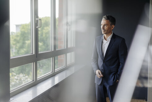 Geschäftsmann im Büro schaut aus dem Fenster - JOSF01375