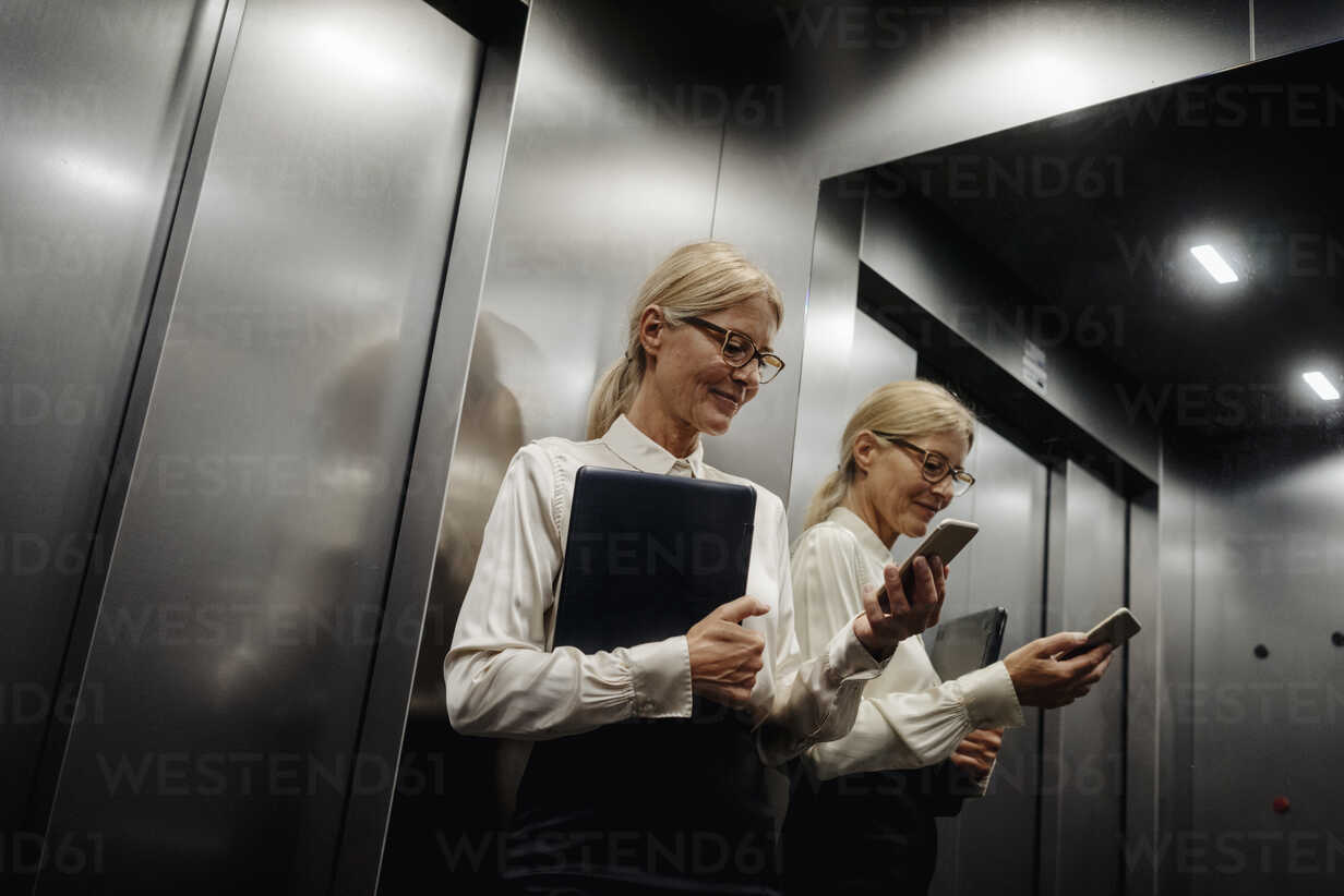 Businesswoman checking cell phone in elevator stock photo