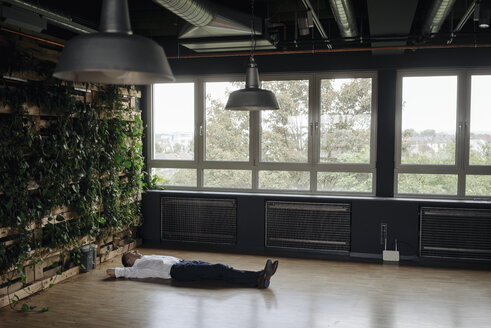 Businessman in green office lying on the floor - JOSF01381