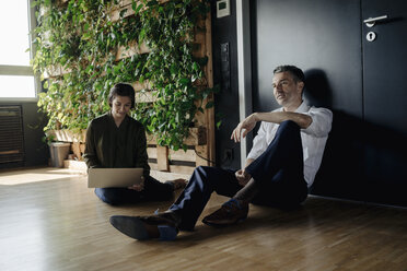 Geschäftsmann und Geschäftsfrau sitzen auf dem Boden in einem grünen Büro und benutzen ein Tablet - JOSF01388