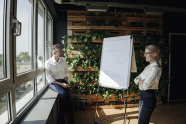 Businessman and businesswoman working with flip chart in green office - JOSF01389