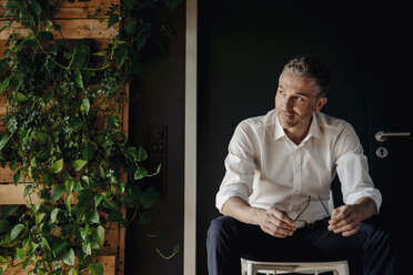 Businessman sitting in green office thinking - JOSF01395