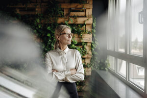 Businesswoman in green office looking out of window - JOSF01405