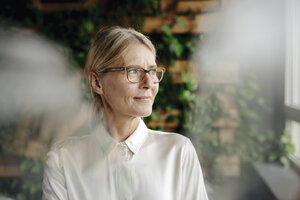 Businesswoman in green office looking out of window - JOSF01407