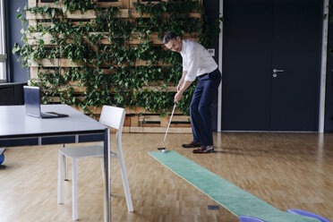 Businessman playing golf in green office - JOSF01410
