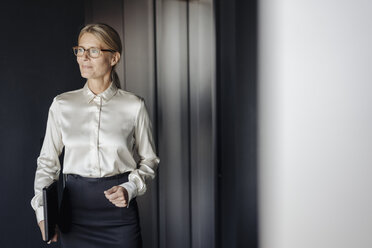 Confident businesswoman in office holding laptop - JOSF01428