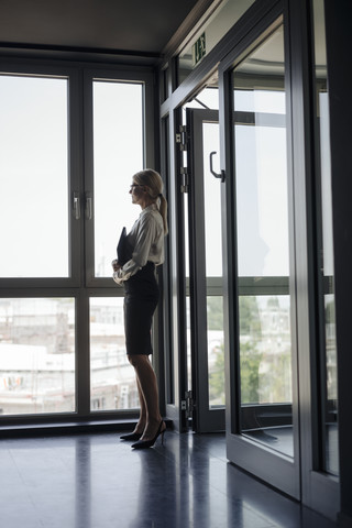 Geschäftsfrau im Büro schaut aus dem Fenster, lizenzfreies Stockfoto