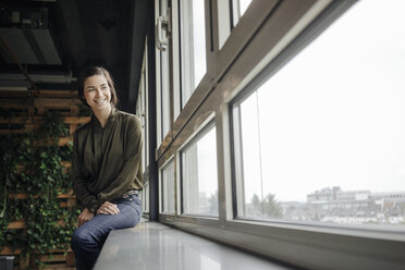 Glückliche junge Frau im Büro, die aus dem Fenster schaut - JOSF01447