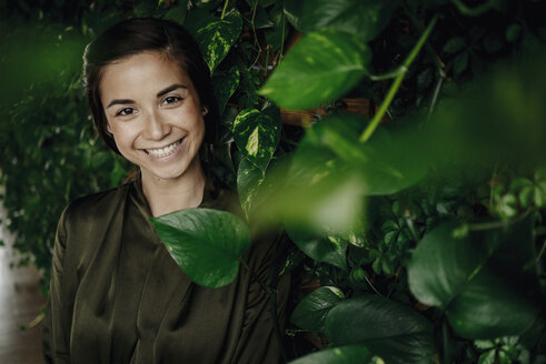 Portait of smiling young woman at wall with climbing plants - JOSF01449