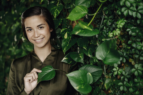 Portait of smiling young woman at wall with climbing plants - JOSF01450