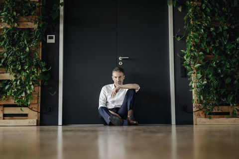 Geschäftsmann sitzt auf dem Boden in einem grünen Büro, lizenzfreies Stockfoto