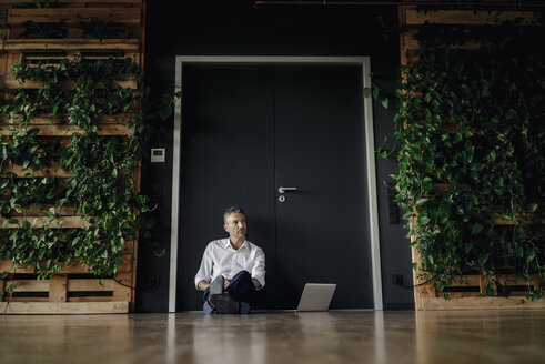Geschäftsmann mit Laptop, der in einem grünen Büro auf dem Boden sitzt - JOSF01458