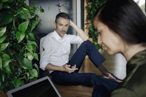 Geschäftsmann und Geschäftsfrau sitzen auf dem Boden in einem grünen Büro und benutzen ein Tablet - JOSF01461