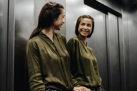 Smiling young woman looking in mirror in elevator stock photo