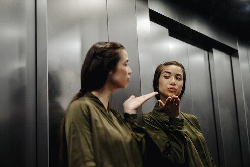 Young woman looking in mirror in elevator blowing a kiss - JOSF01486