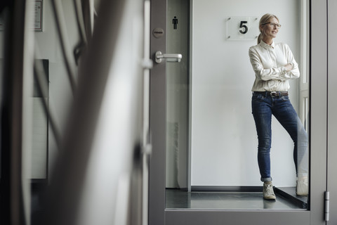 Businesswoman standing on the corridor looking out of window stock photo