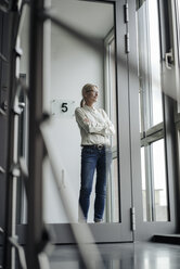 Geschäftsfrau steht auf dem Flur und schaut aus dem Fenster - JOSF01488