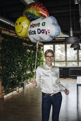 Smiling businesswoman in green office holding balloon - JOSF01499